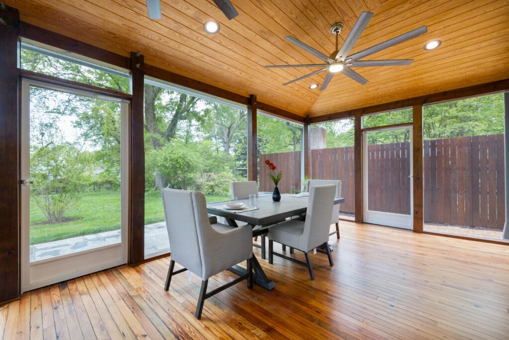 Contemporary dining room with large windows and wooden ceiling, overlooking a lush garden.